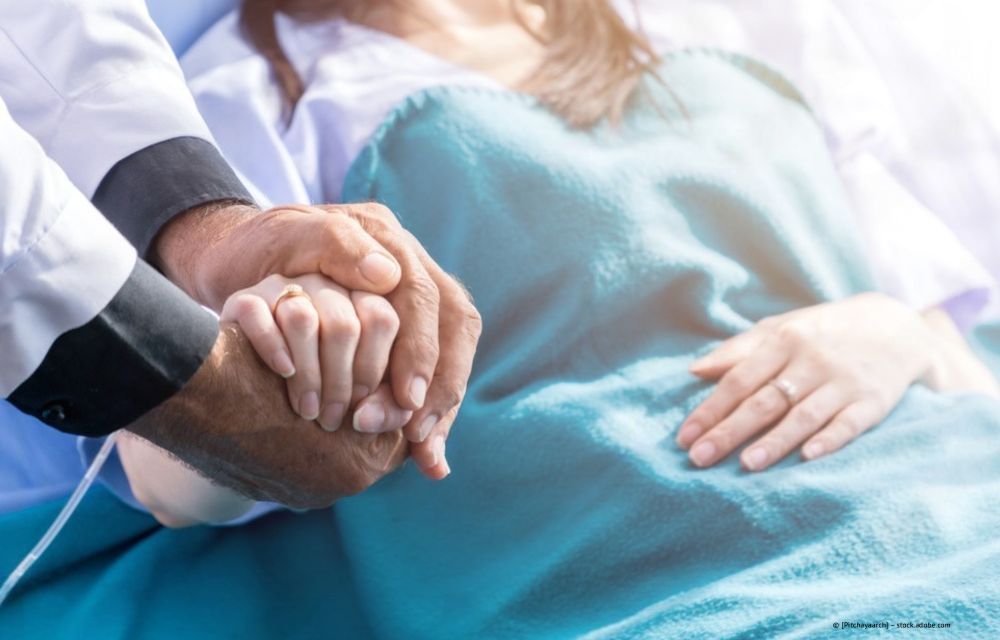 Eine Pflegekraft in blauer Kleidung unterhält sich mit einer lächelnden älteren Dame, die draußen auf einer Veranda sitzt.