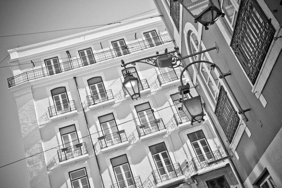 Fotografia em preto e branco de um edifício com varandas e janelas em arco, com postes de iluminação em primeiro plano.