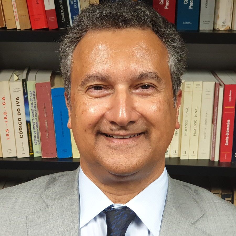 Um homem de terno sorri em frente a uma estante repleta de livros.