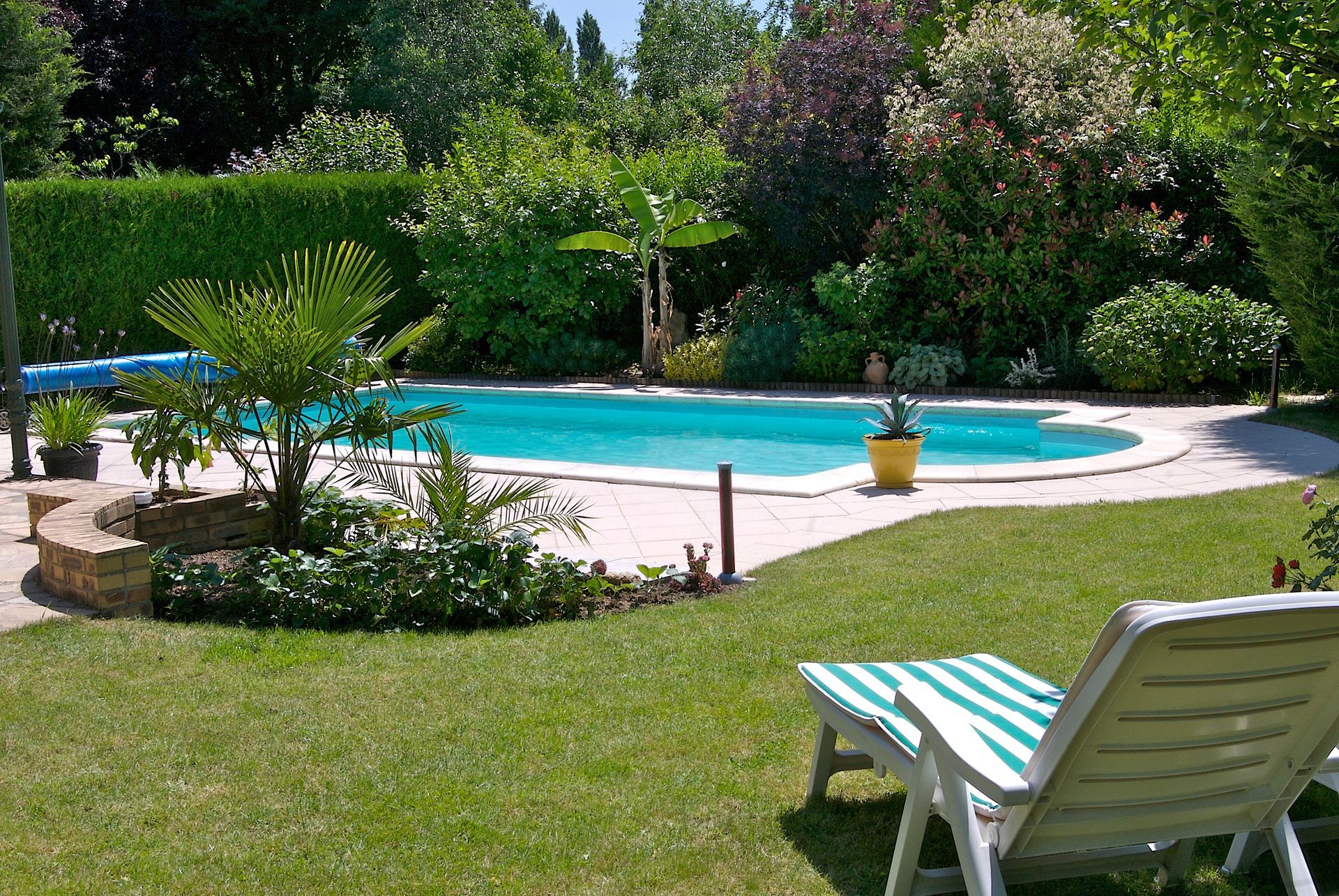 Une piscine entourée d'une pelouse verdoyante et d'arbres, avec une chaise longue au premier plan.