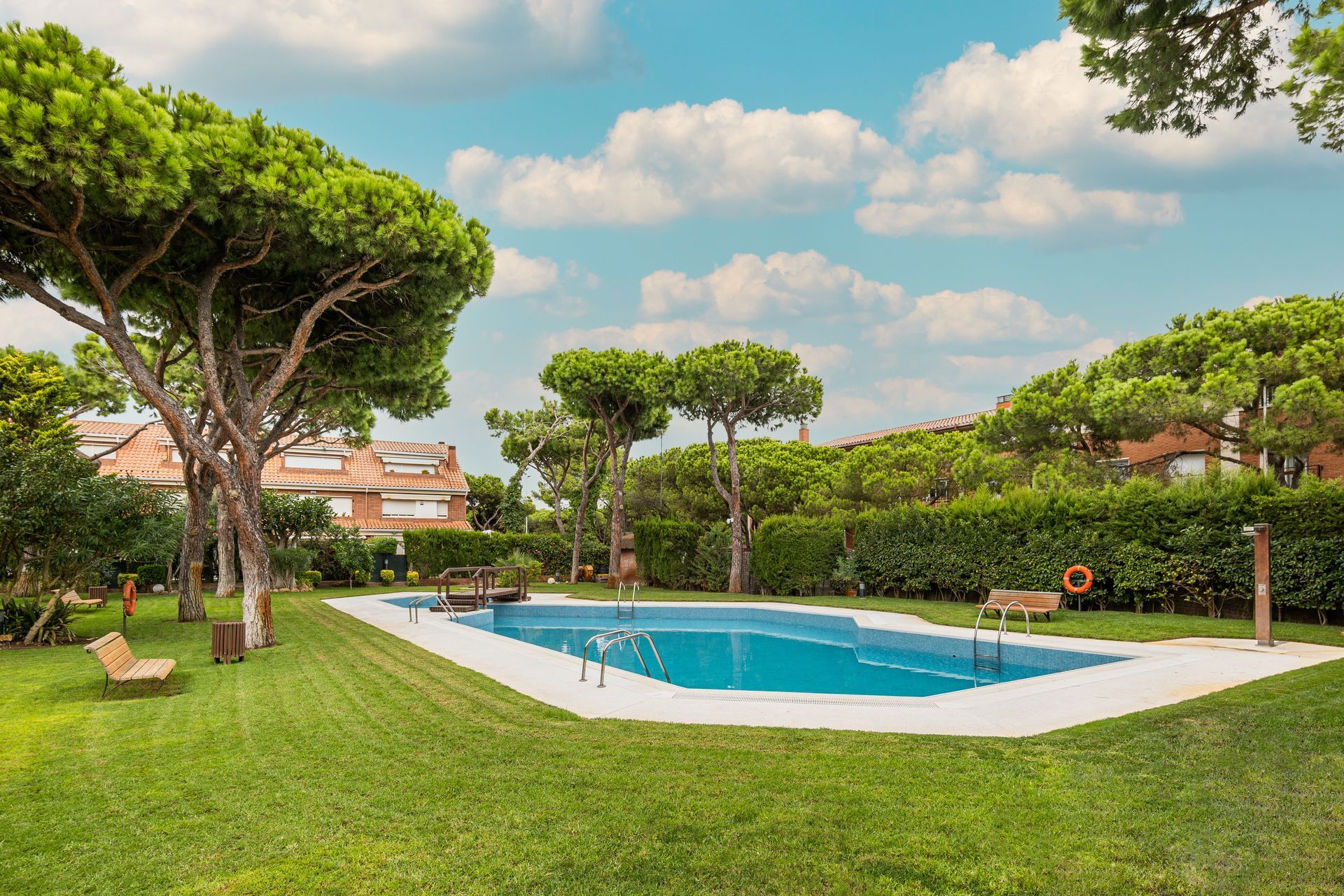 Une piscine entourée de pelouses et d'arbres sous un ciel bleu.