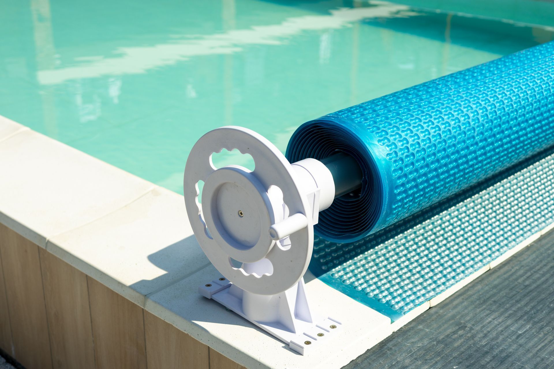 Couverture de piscine à bulles enroulée sur un enrouleur fixé près de la piscine.