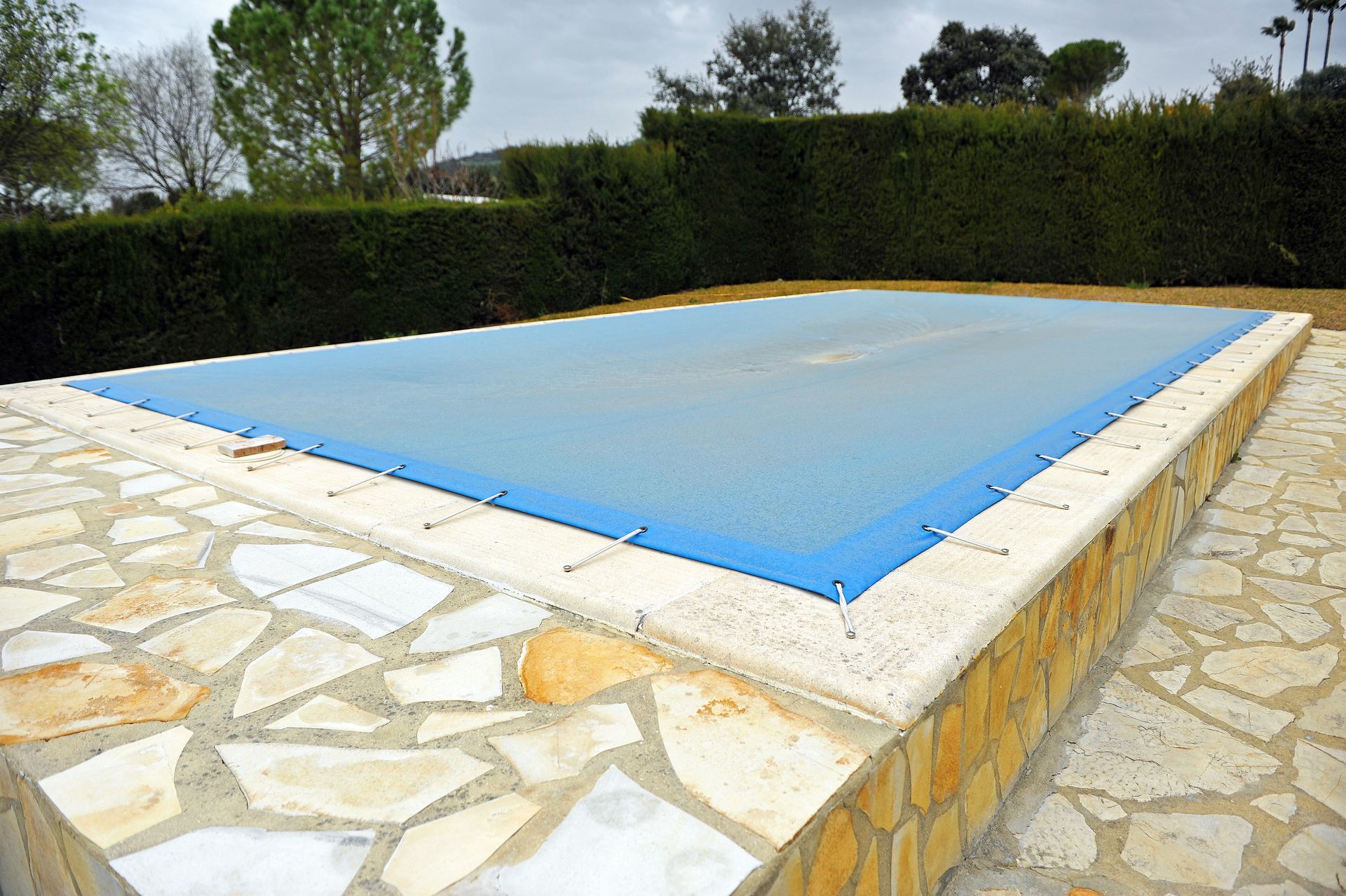 Couverture de piscine bleue sur une piscine rectangulaire entourée d'une terrasse en pierre.