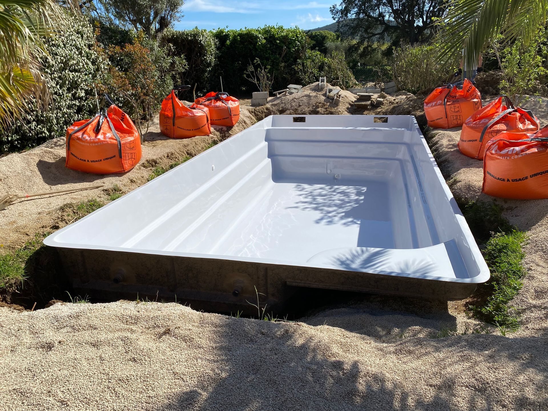Piscine coque en cours d'installation dans un jardin.