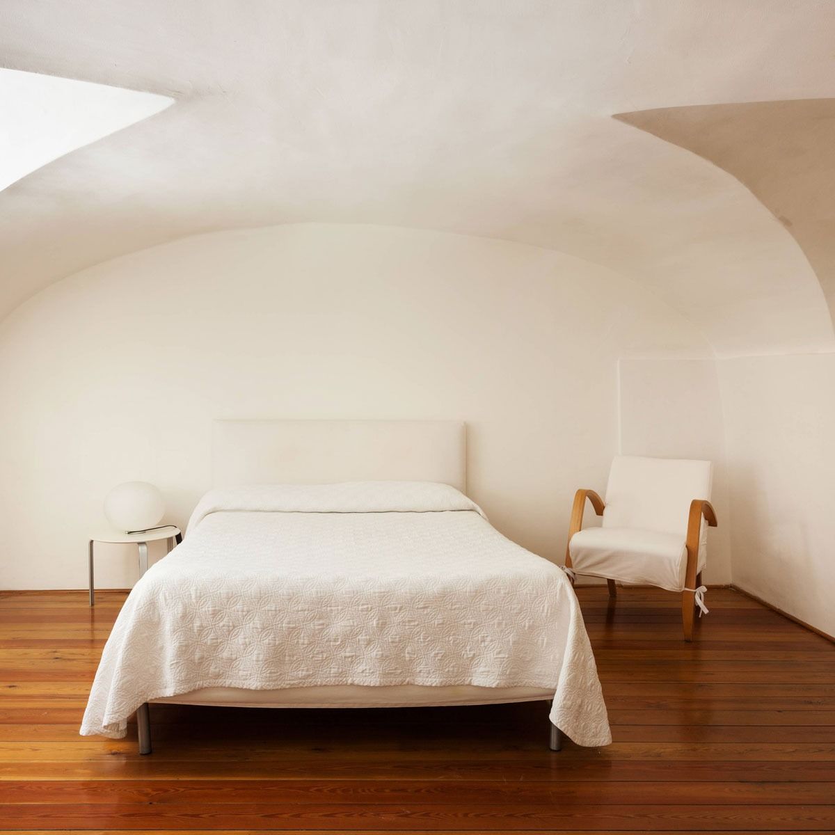 Un dormitorio con una cama, una silla y una ventana.