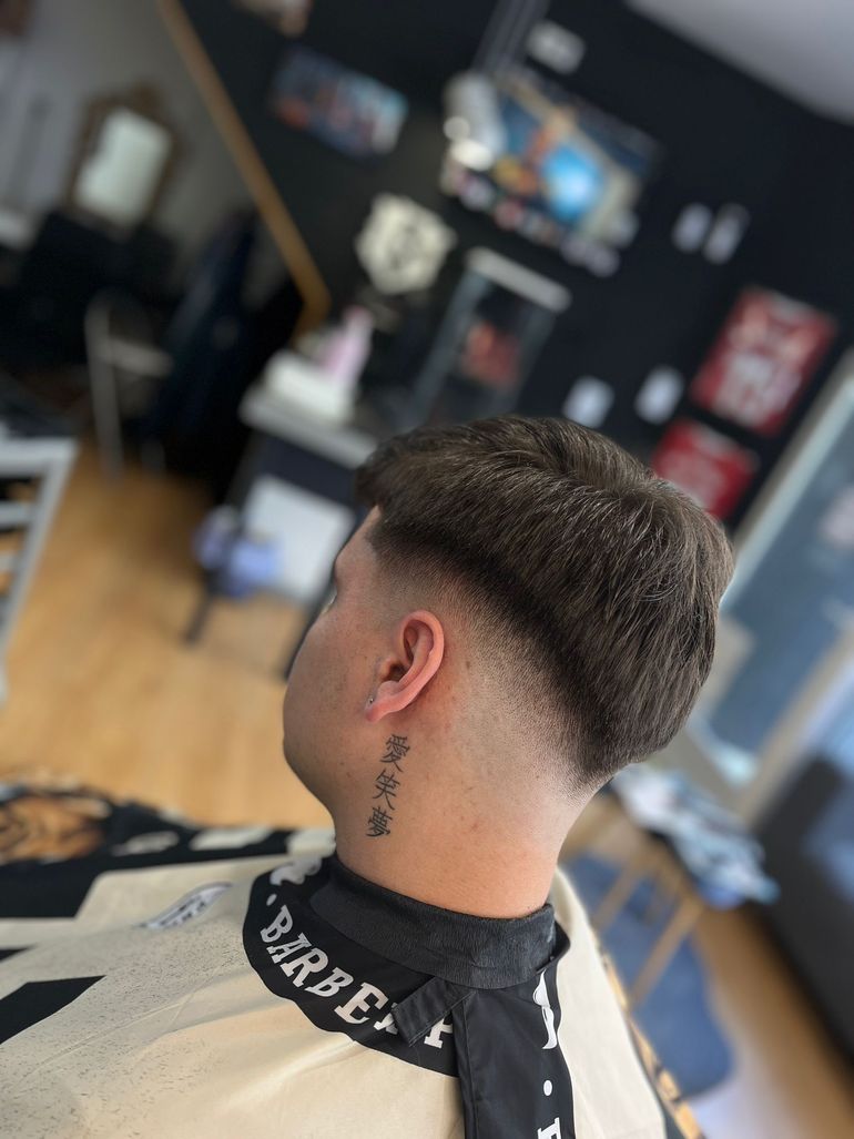 Un hombre con un tatuaje en el cuello se está cortando el pelo en un barbero.