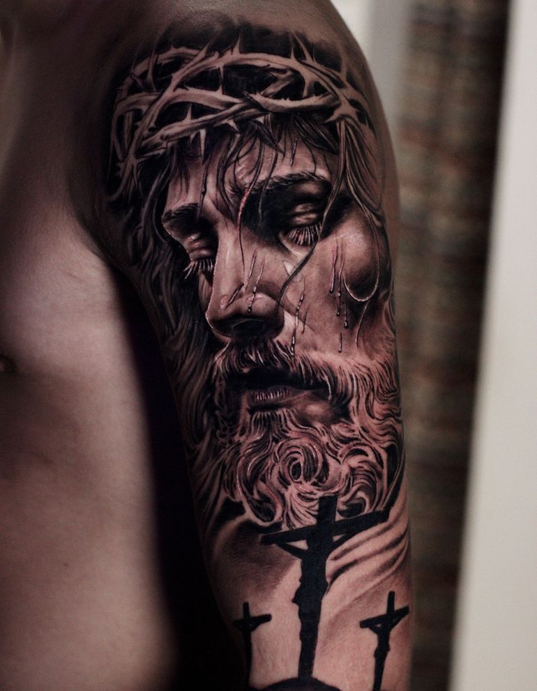 Un hombre tiene un tatuaje de Jesús con una corona de espinas en su brazo.
