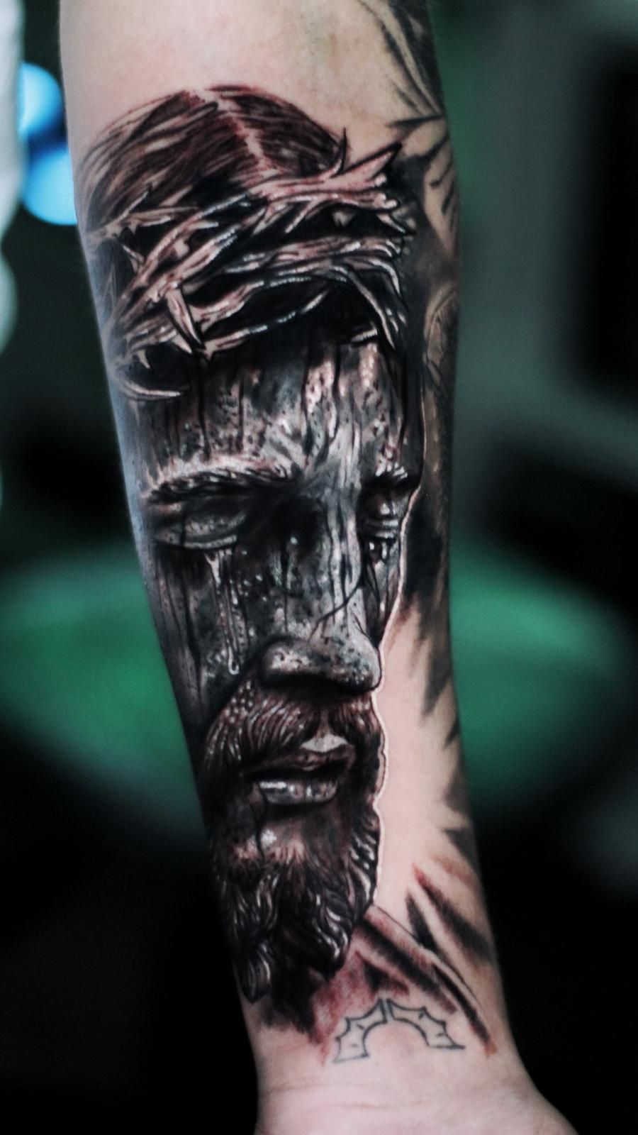 Un hombre tiene un tatuaje de Jesús con una corona de espinas en su antebrazo.
