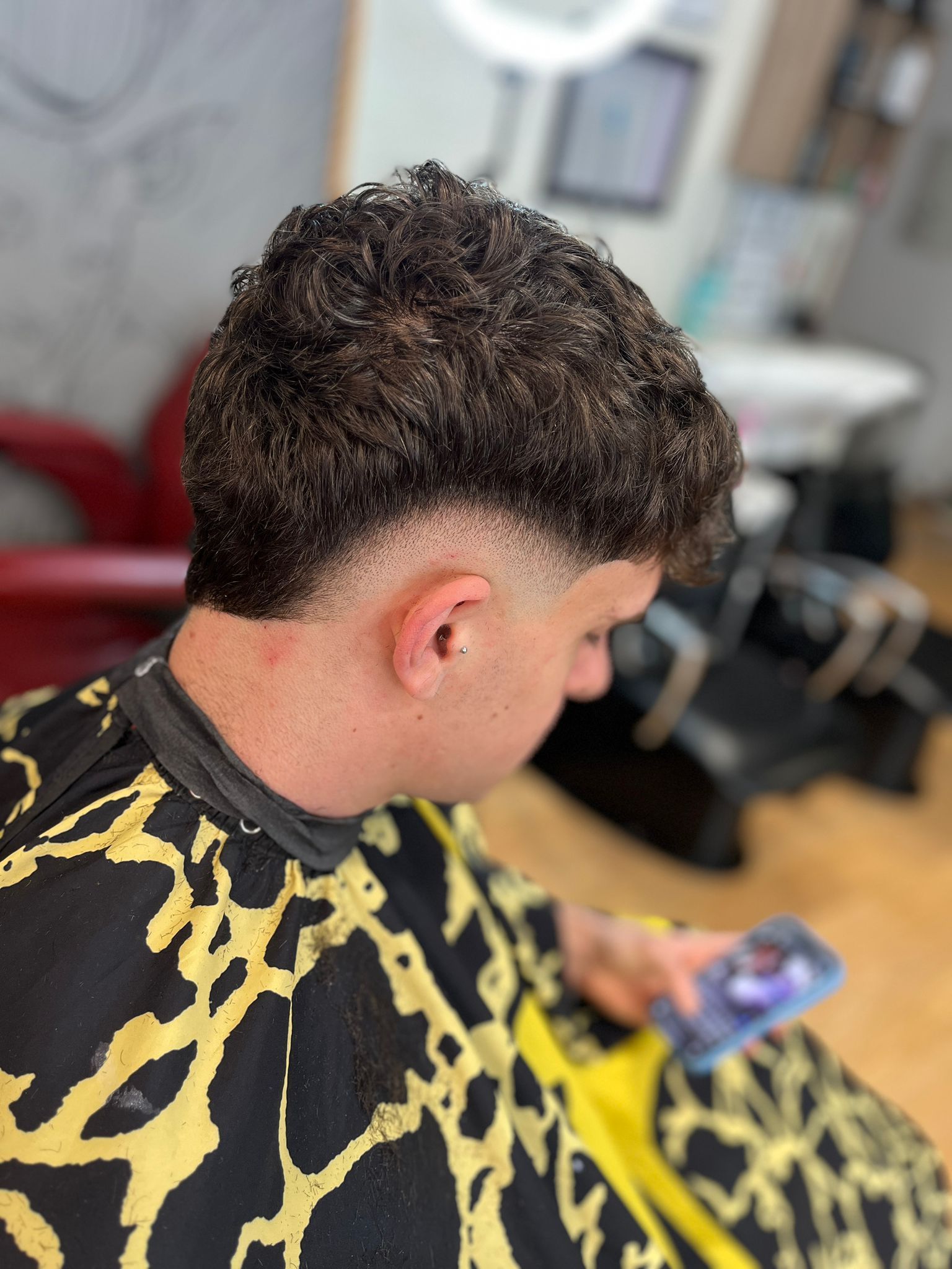 Un hombre se está cortando el pelo en una barbería mientras mira su teléfono.
