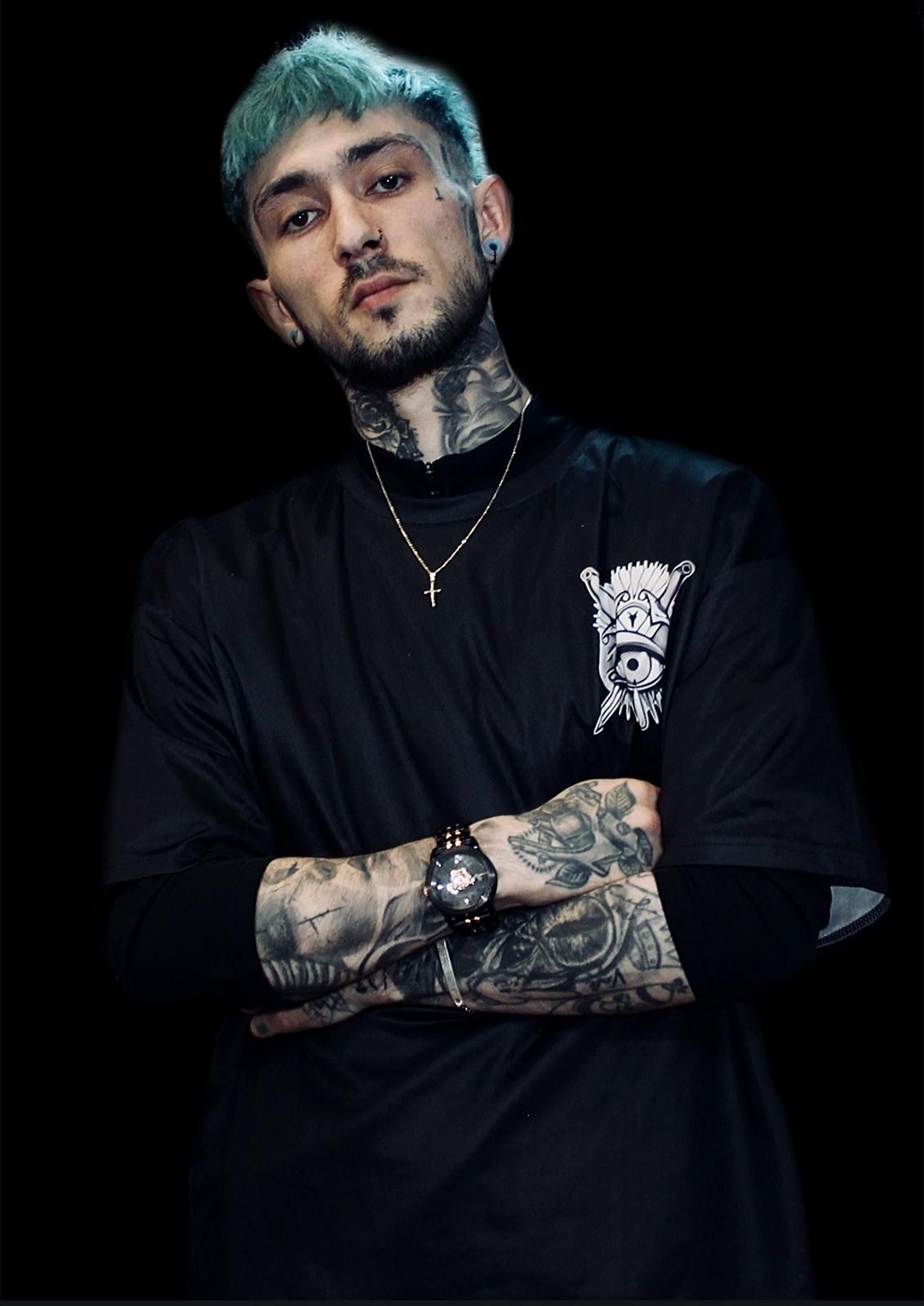 Un hombre con cabello verde y tatuajes lleva una camisa negra y un reloj.