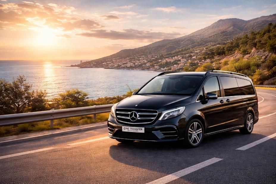 Una furgoneta Mercedes-Benz Clase V negra circulando por una carretera costera al atardecer