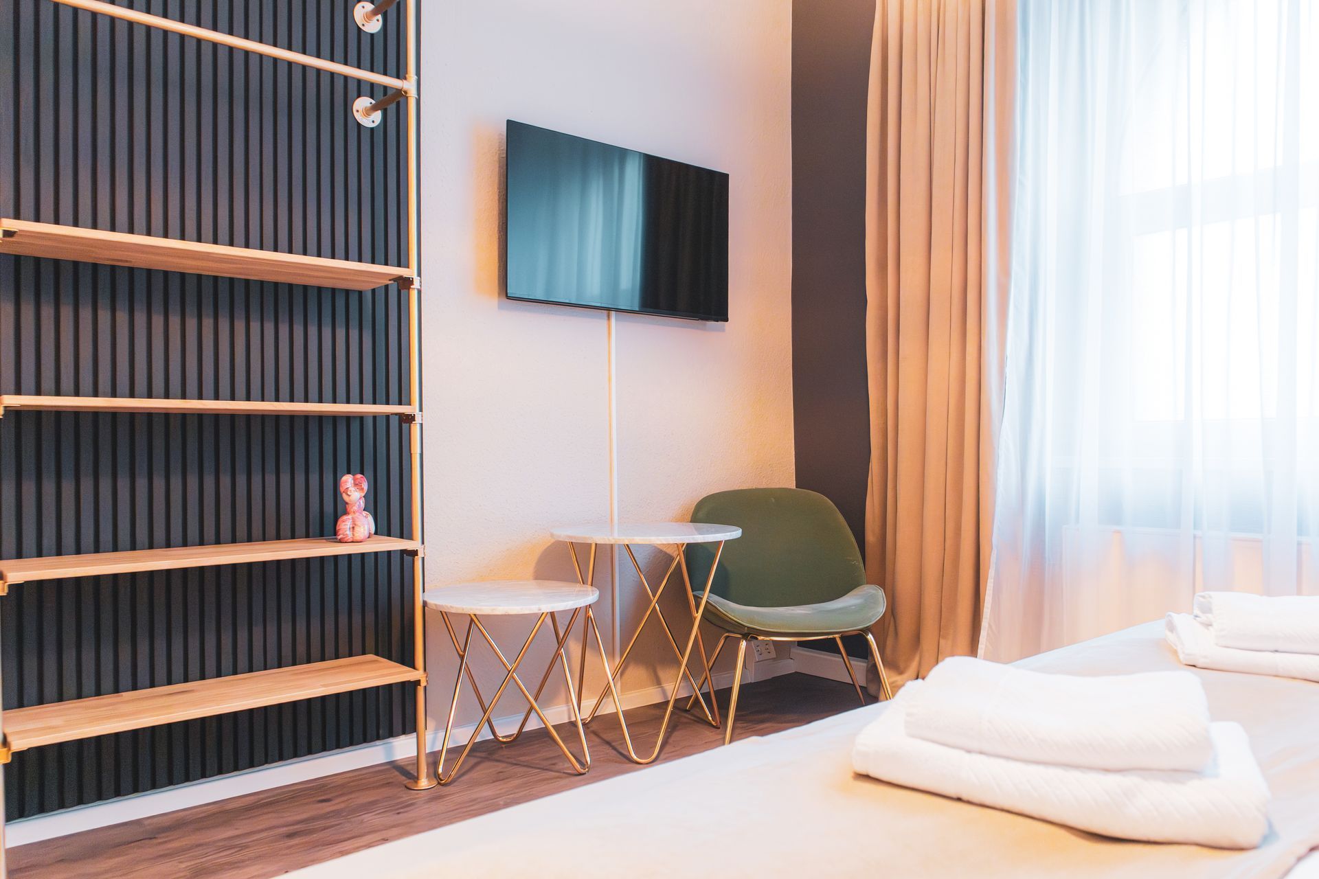 Blick auf ein Regal-System, einen Sessel und kleine Tische in einem modernen Hotelzimmer.