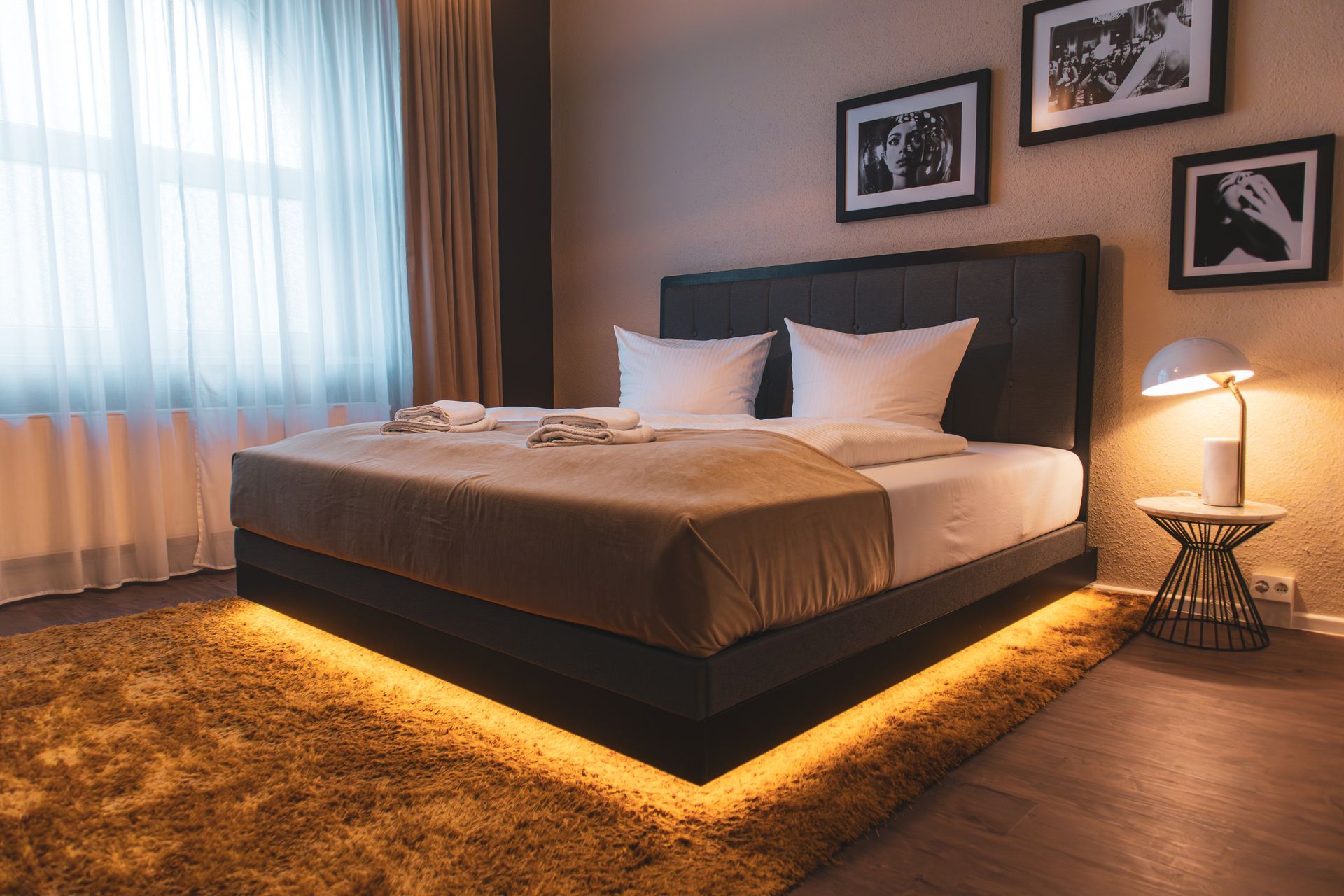 Modernes Doppelbett mit warmem LED-Lichtband am Boden, schwarzen Bildern an der Wand und stilvoller Nachttischlampe.