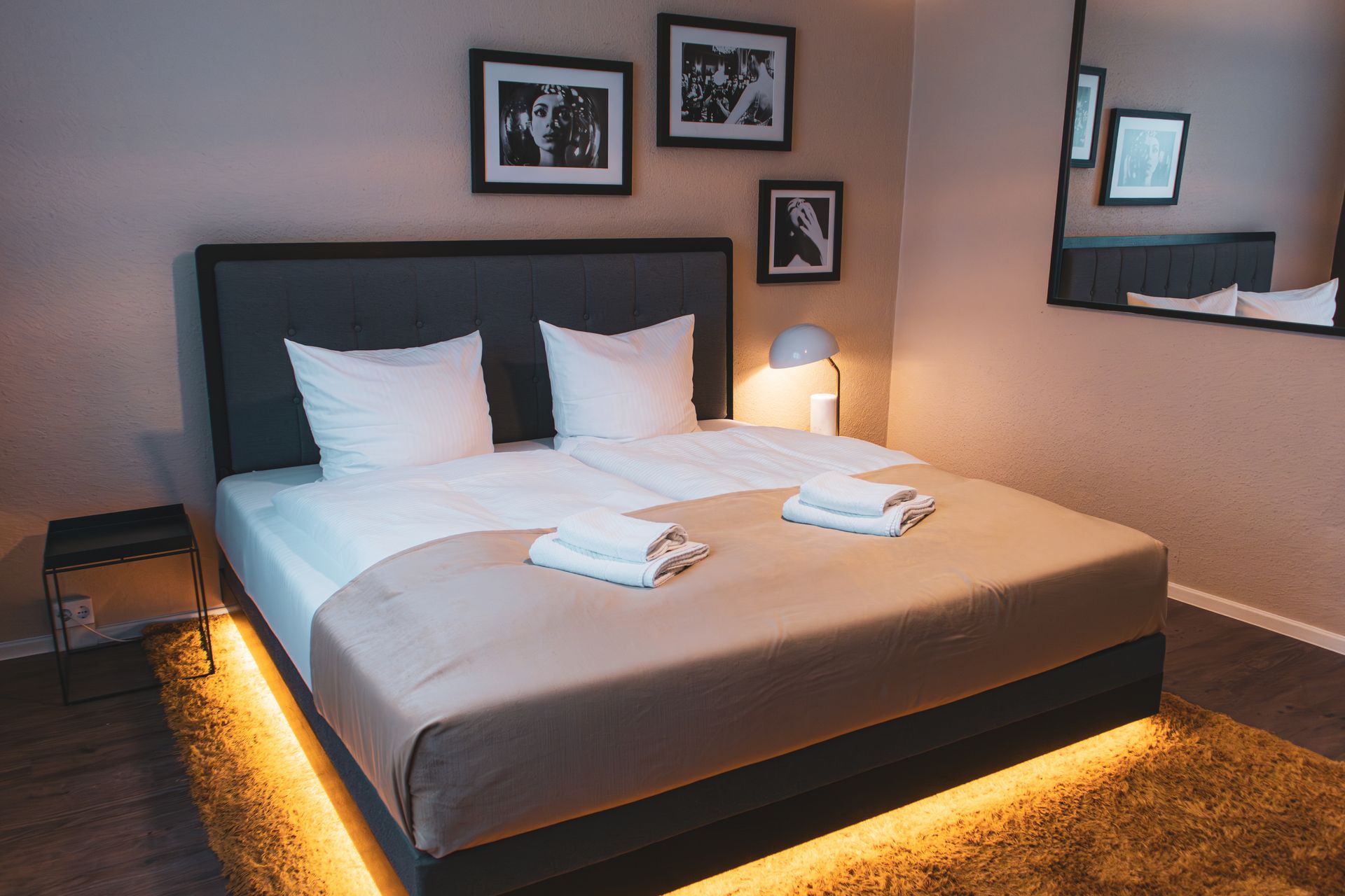 Gemachtes Hotel-Doppelbett mit beleuchtetem Sockel und seitlichem Nachttisch.