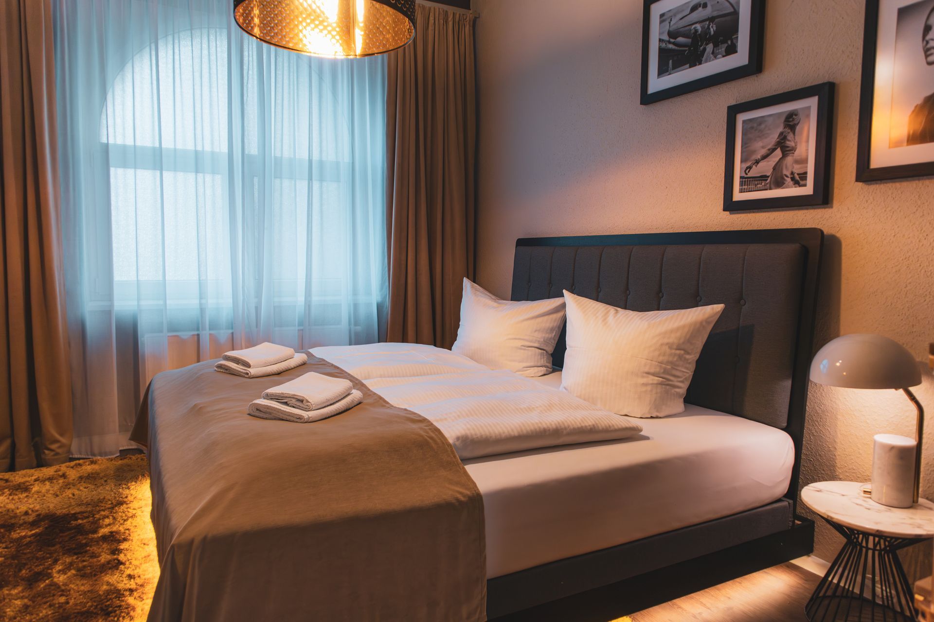 Gemütliches Hotelzimmer mit Doppelbett vor einem großen Fenster mit hellen Vorhängen.