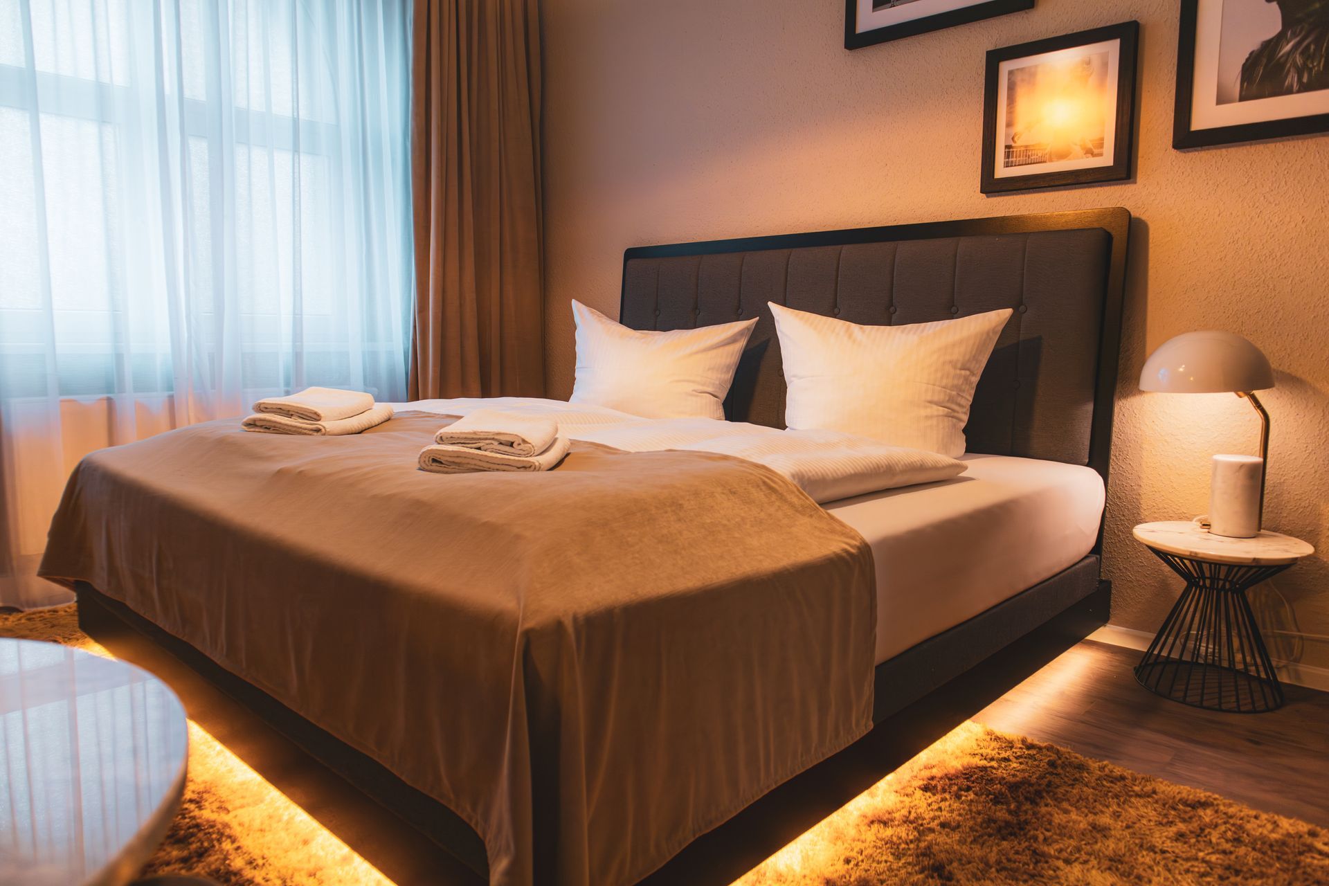 Perspektivische Ansicht eines Doppelbetts mit brauner Tagesdecke und indirektem Licht.