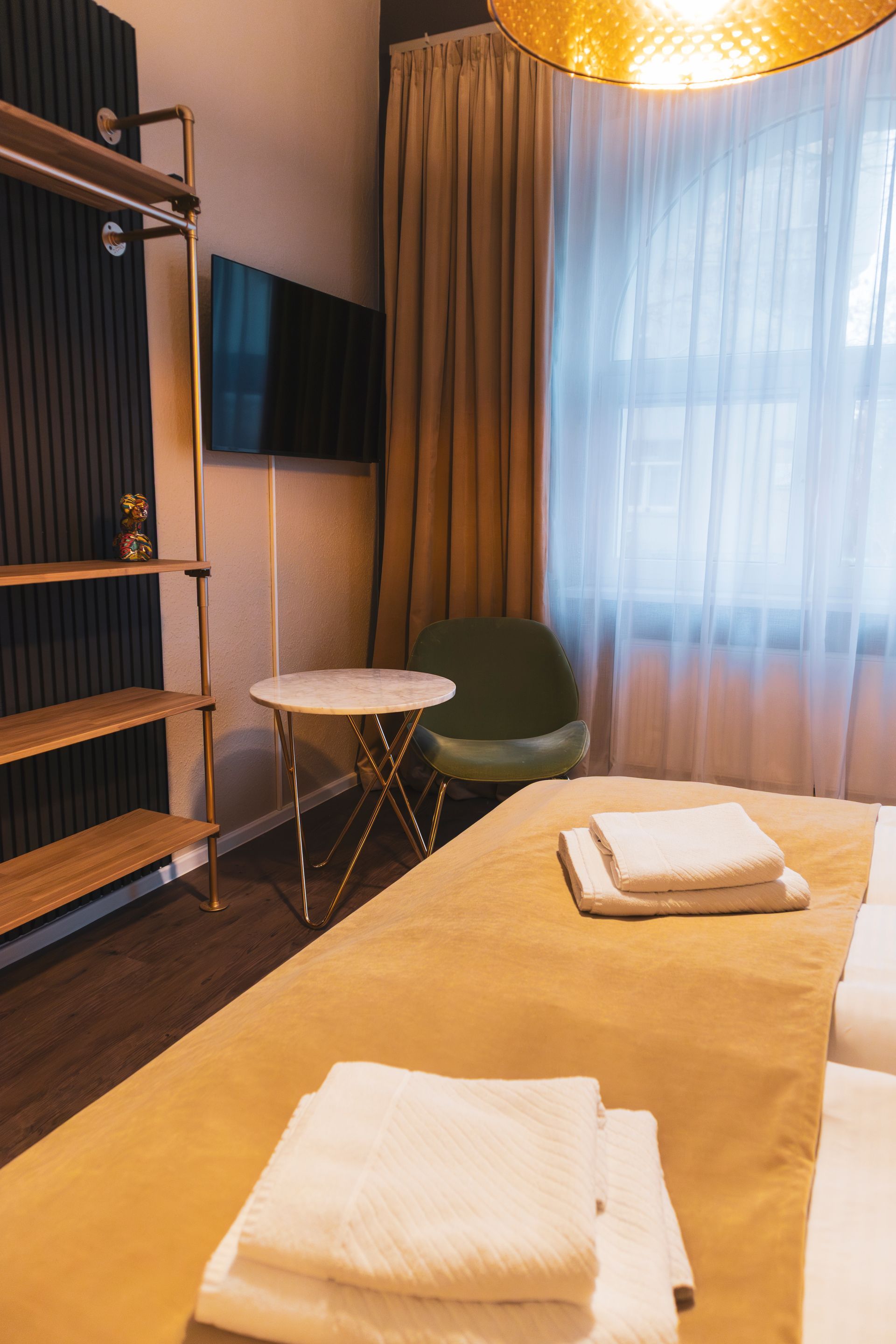 Wand-TV und helle Vorhänge neben einer dekorativen goldenen Deckenleuchte.