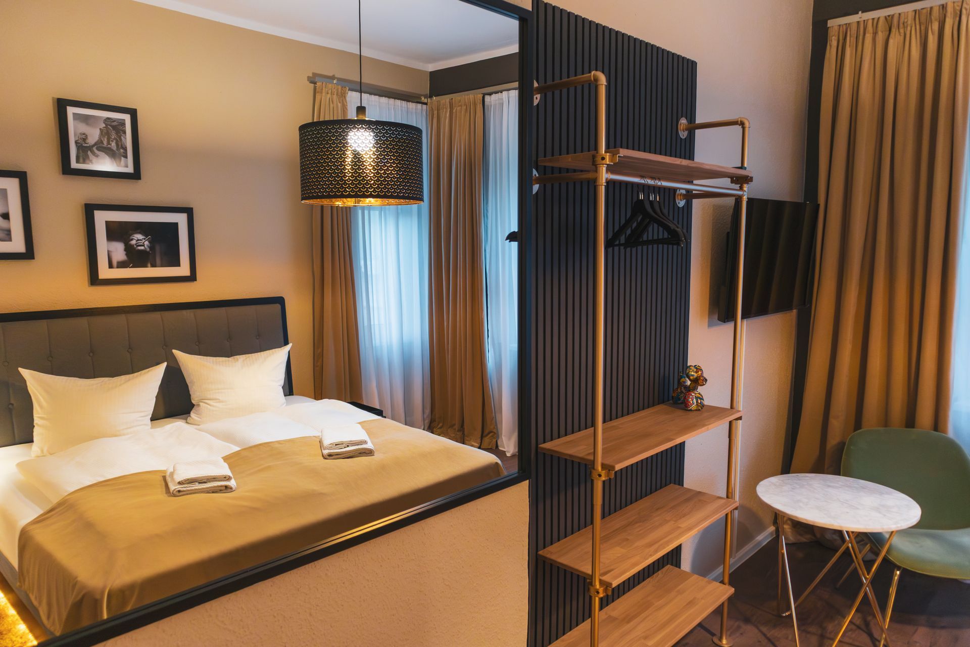 Raumansicht mit Bett, hängender Design-Lampe und einem offenen Kleiderregal aus Holz und Metall.