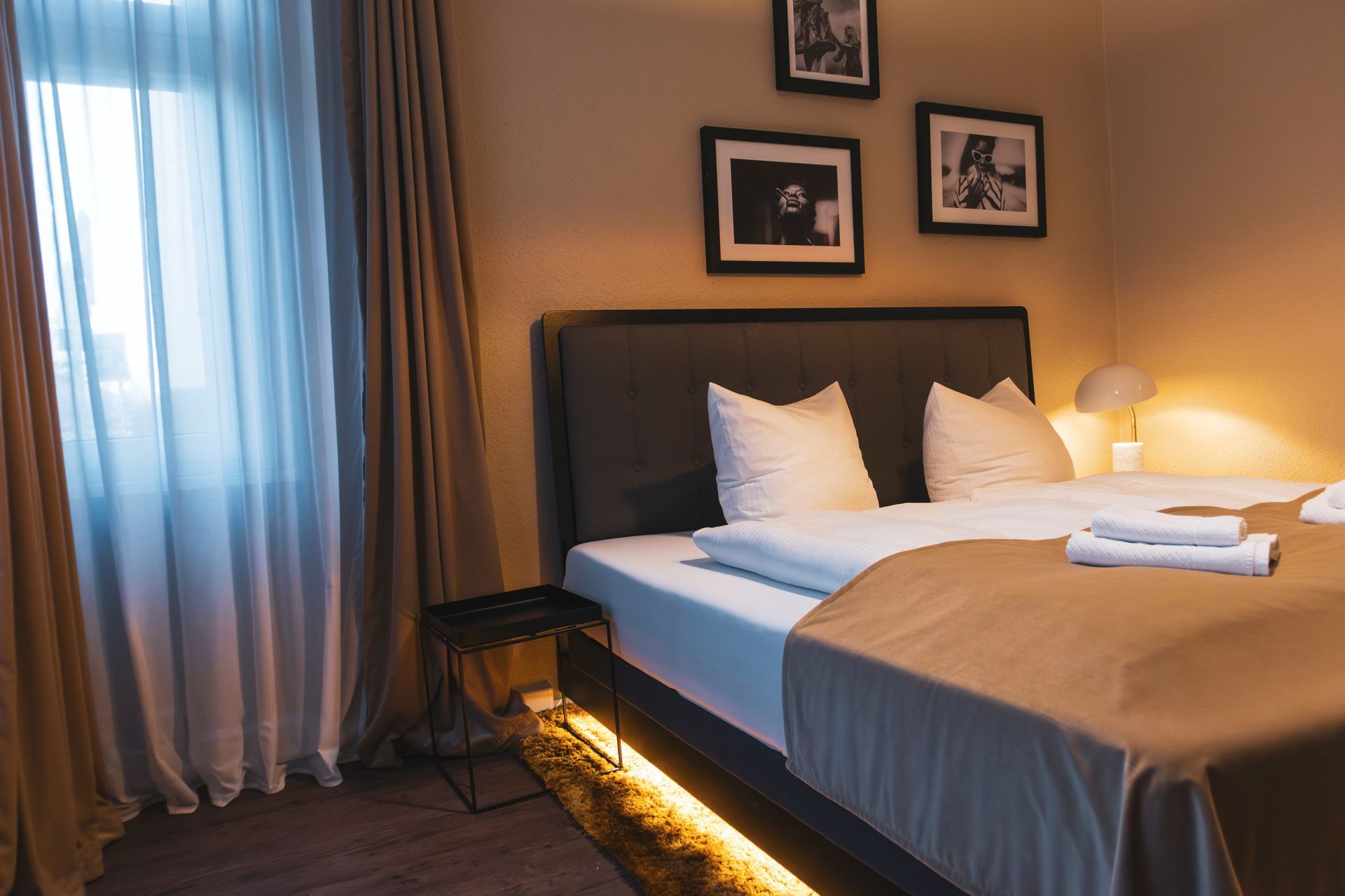 Gemütliches Doppelbett in warmem Licht mit Blick Richtung Fenster.