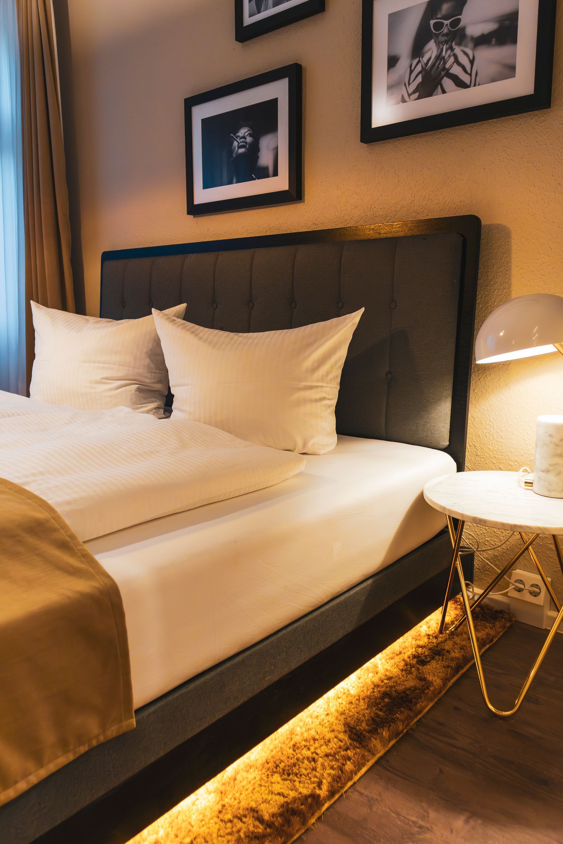 Nahaufnahme eines dunklen Bett-Kopfteils vor einer Wand mit Schwarz-Weiß-Fotografien.