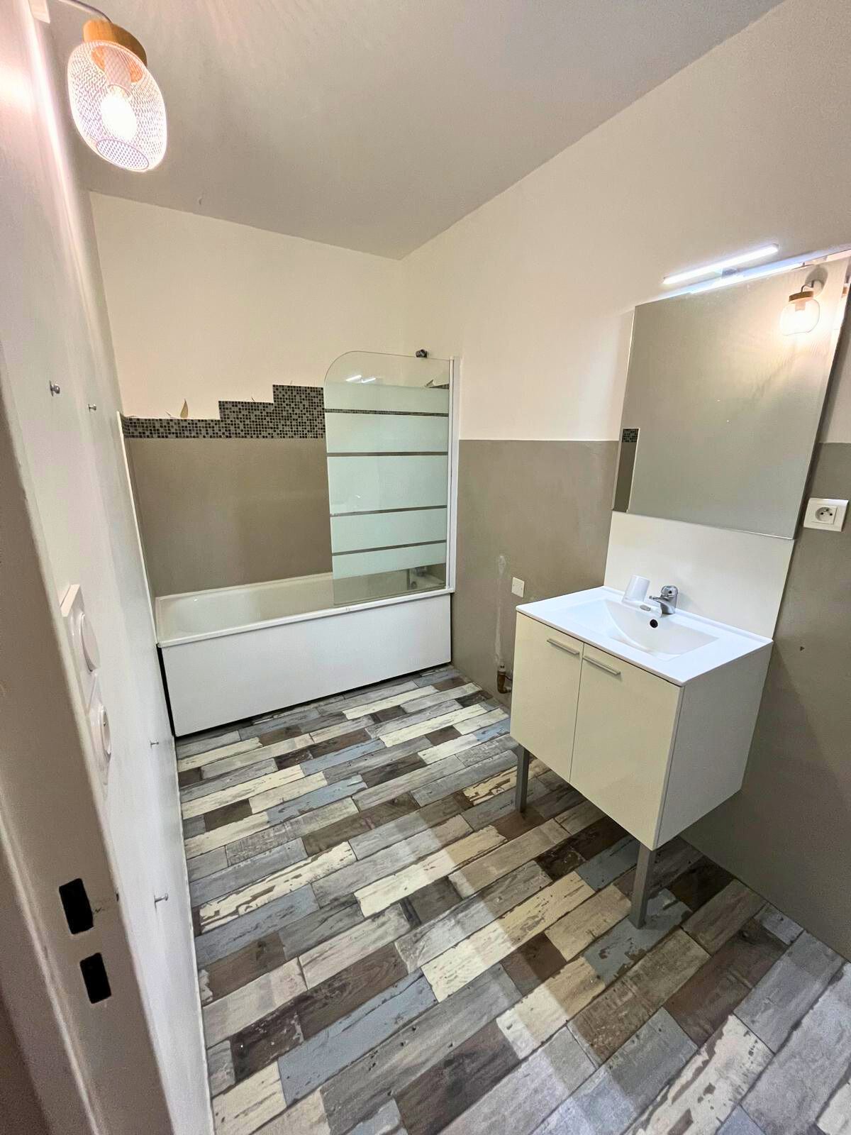 Salle de bains avec évier, miroir et baignoire au fond