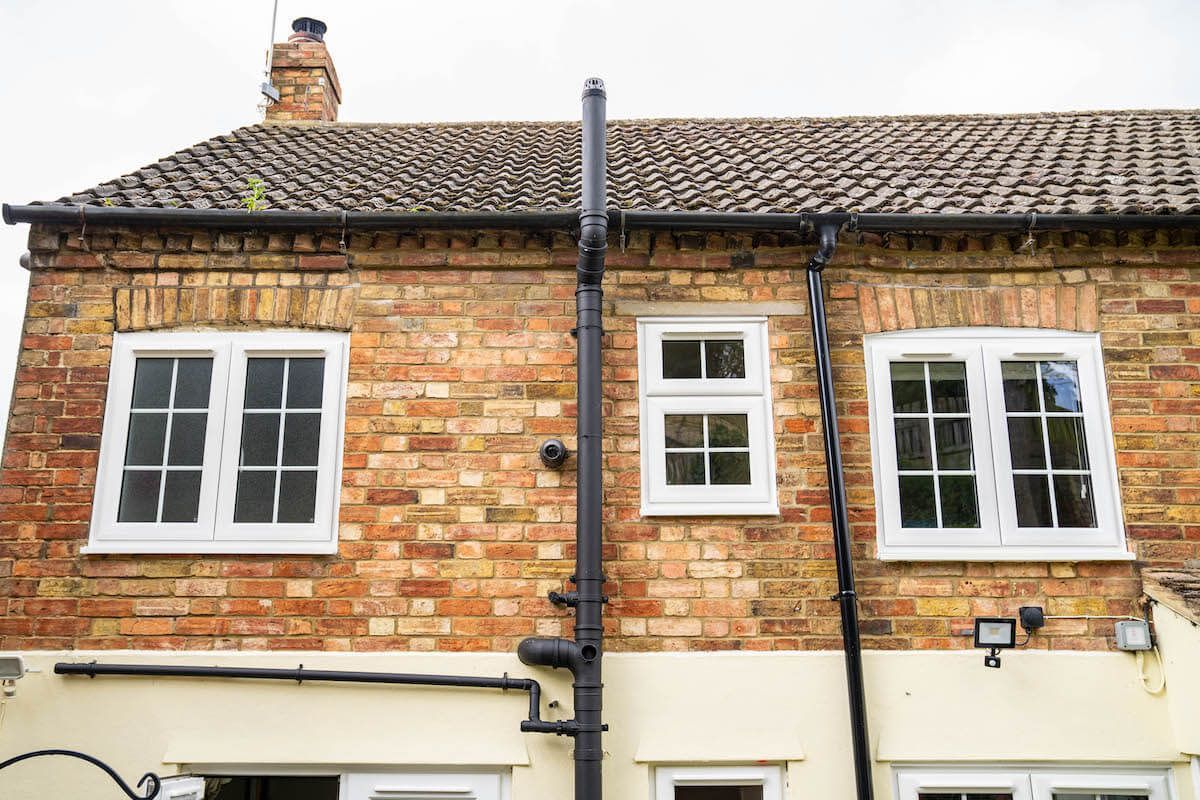 A brick house with white windows and a chimney on the roof.