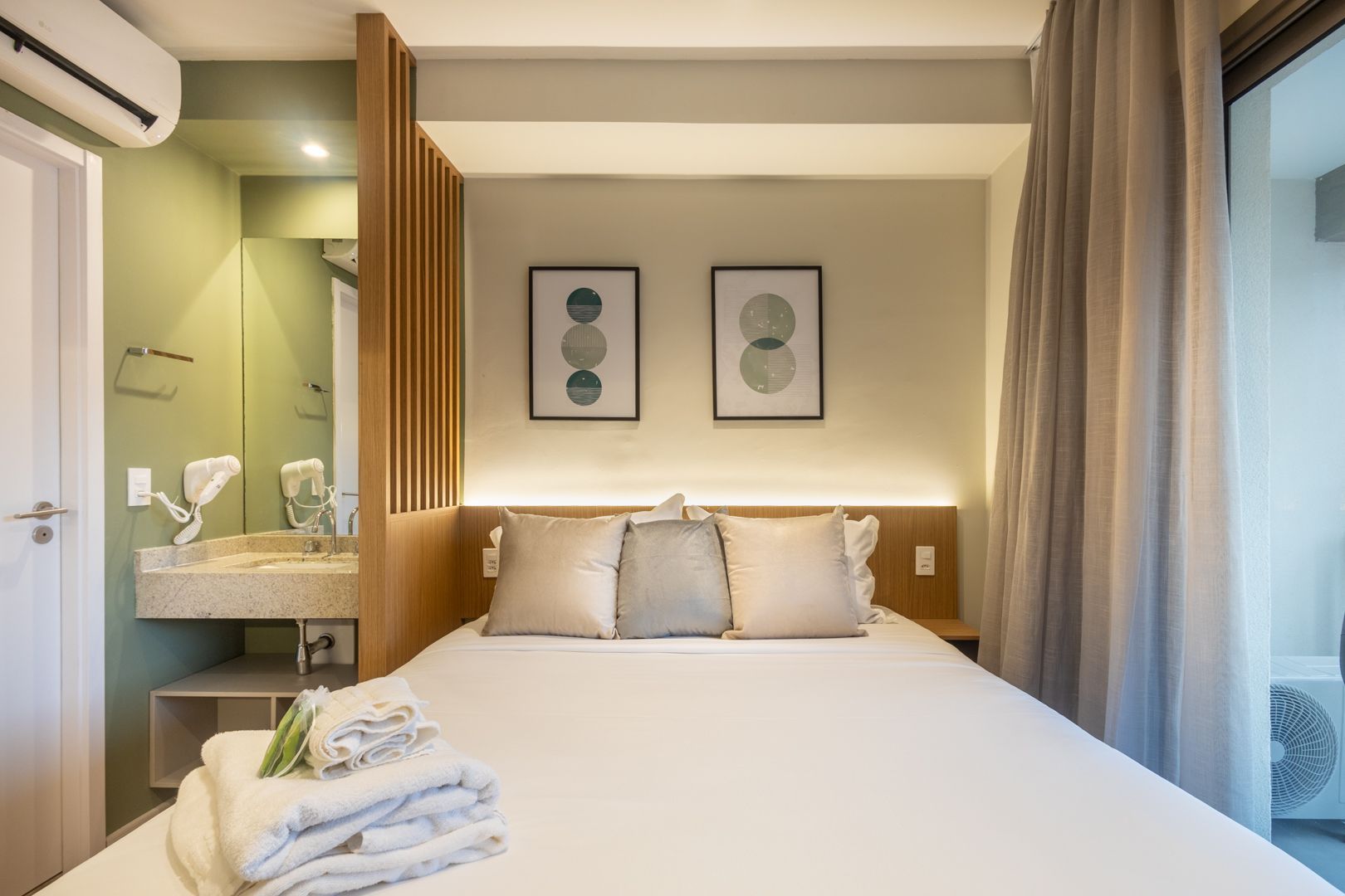 Quarto moderno com cama branca impecavelmente arrumada, obras de arte emolduradas, pia embutida e portas de vidro deslizantes.