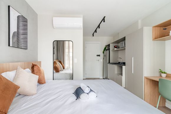 Quarto minimalista branco com cama, espelho, obras de arte na parede e escrivaninha com prateleiras embutidas.