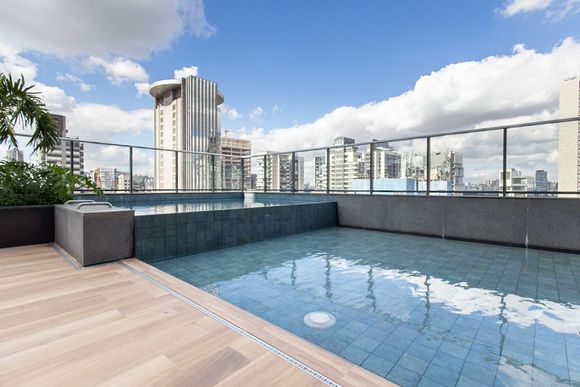 Piscina na cobertura com vista para o horizonte da cidade, guarda-corpo de vidro e deck de madeira clara.