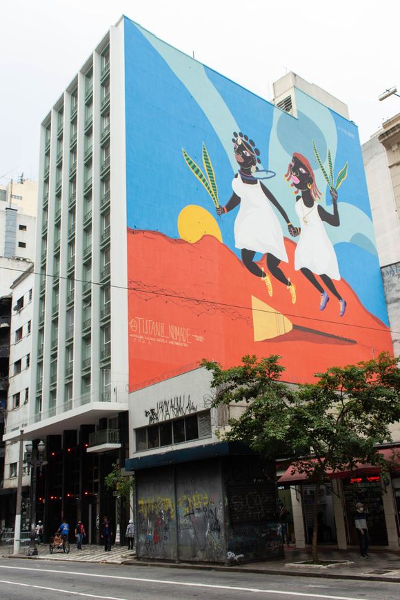 Mural de rua retratando duas pessoas pulando em um prédio de vários andares com fundo geométrico azul e laranja.