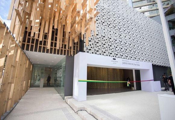 Entrada de edifício moderno com ripas de madeira, parede branca estampada e faixa verde neon no balcão.