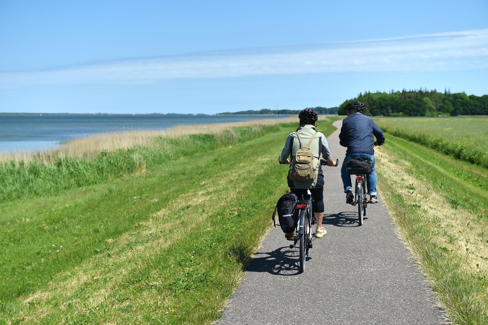 Zwei Personen fahren mit dem Fahrrad einen Weg in der Nähe eines Gewässers entlang