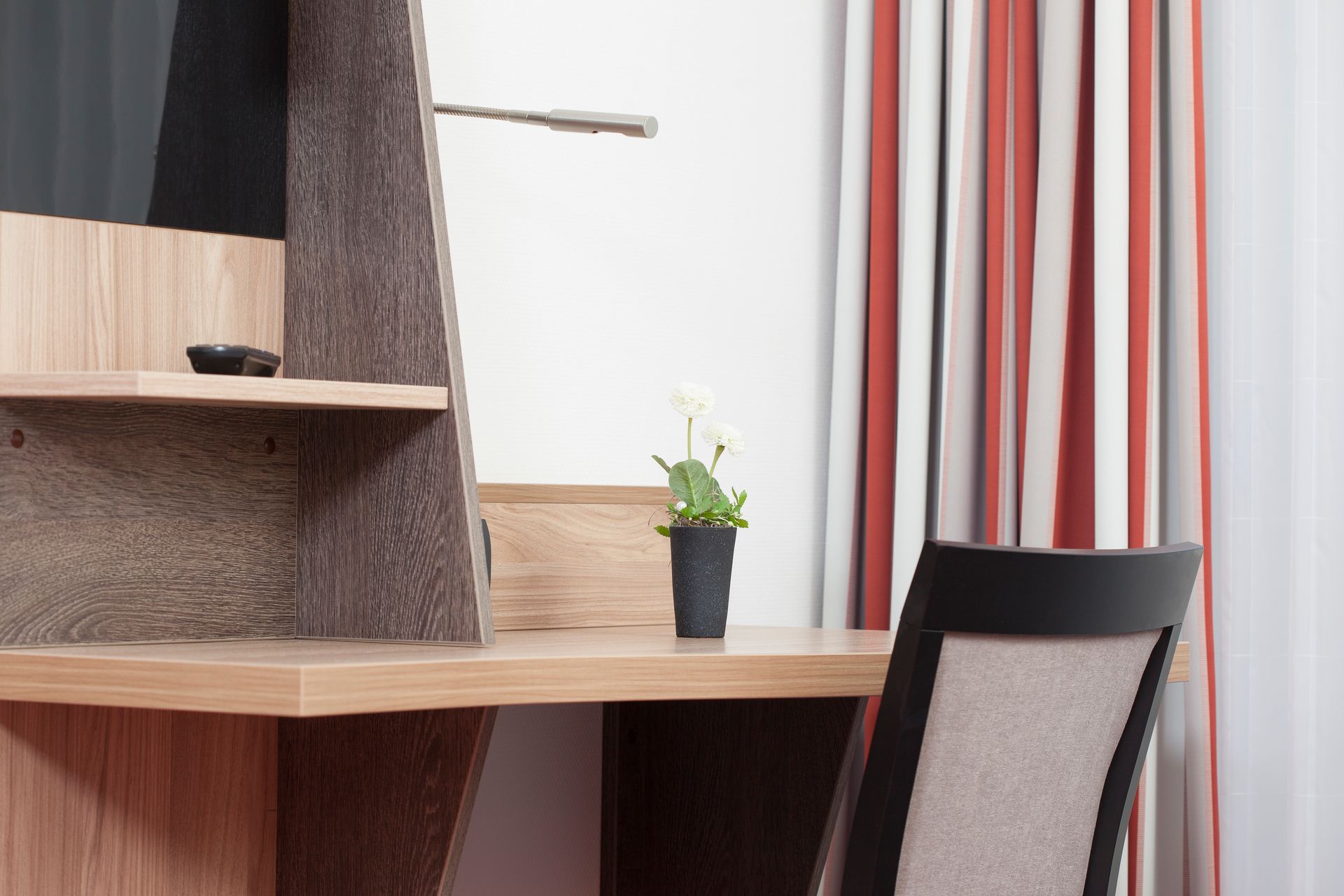 Ein Schreibtisch mit einer Topfpflanze darauf und einem Stuhl in einem Hotelzimmer.