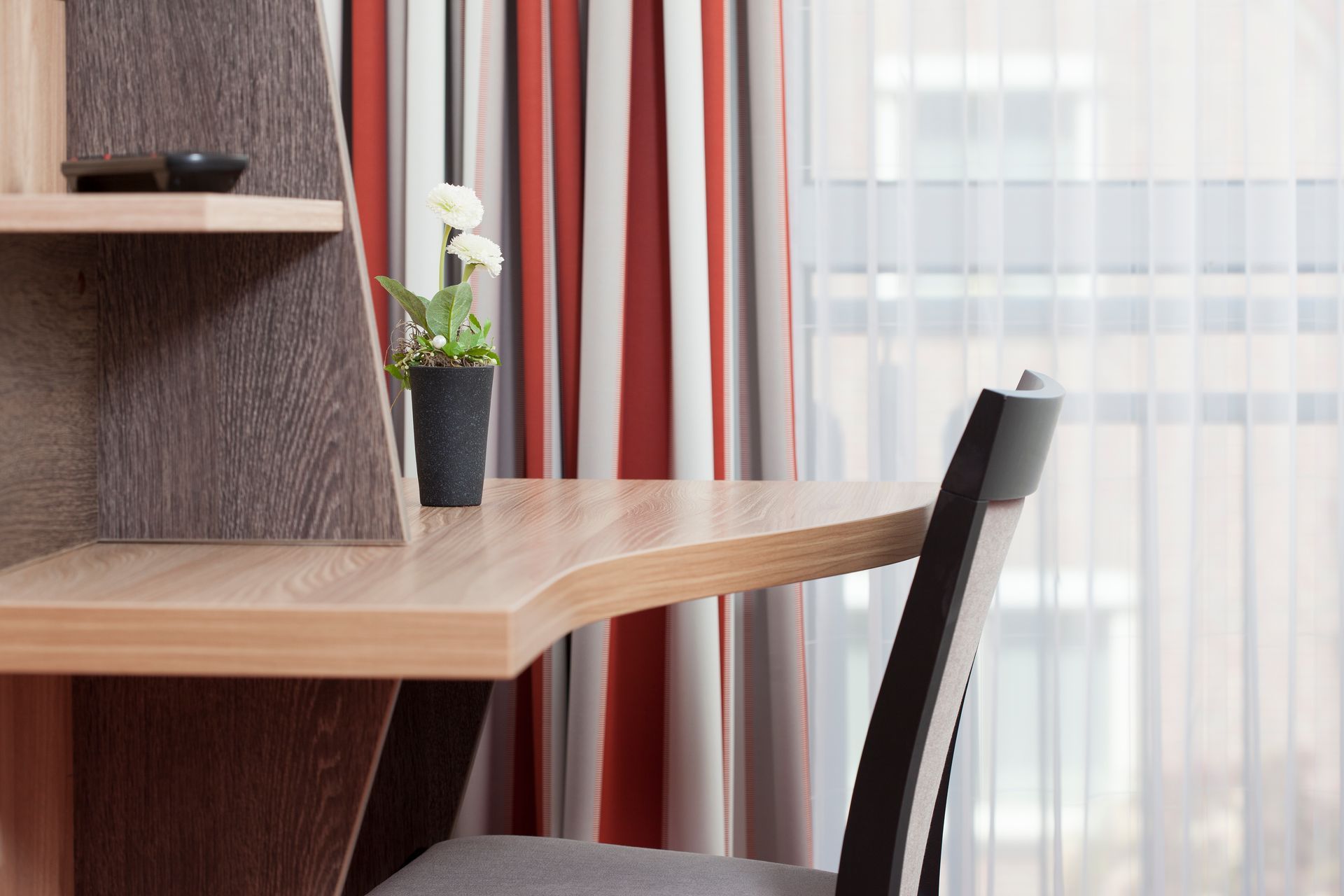 Ein Schreibtisch mit einem Stuhl und einer Vase mit Blumen darauf in einem Hotelzimmer.