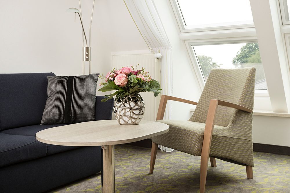 Ein Wohnzimmer mit Sofa, Sessel, Tisch und Blumenvase.