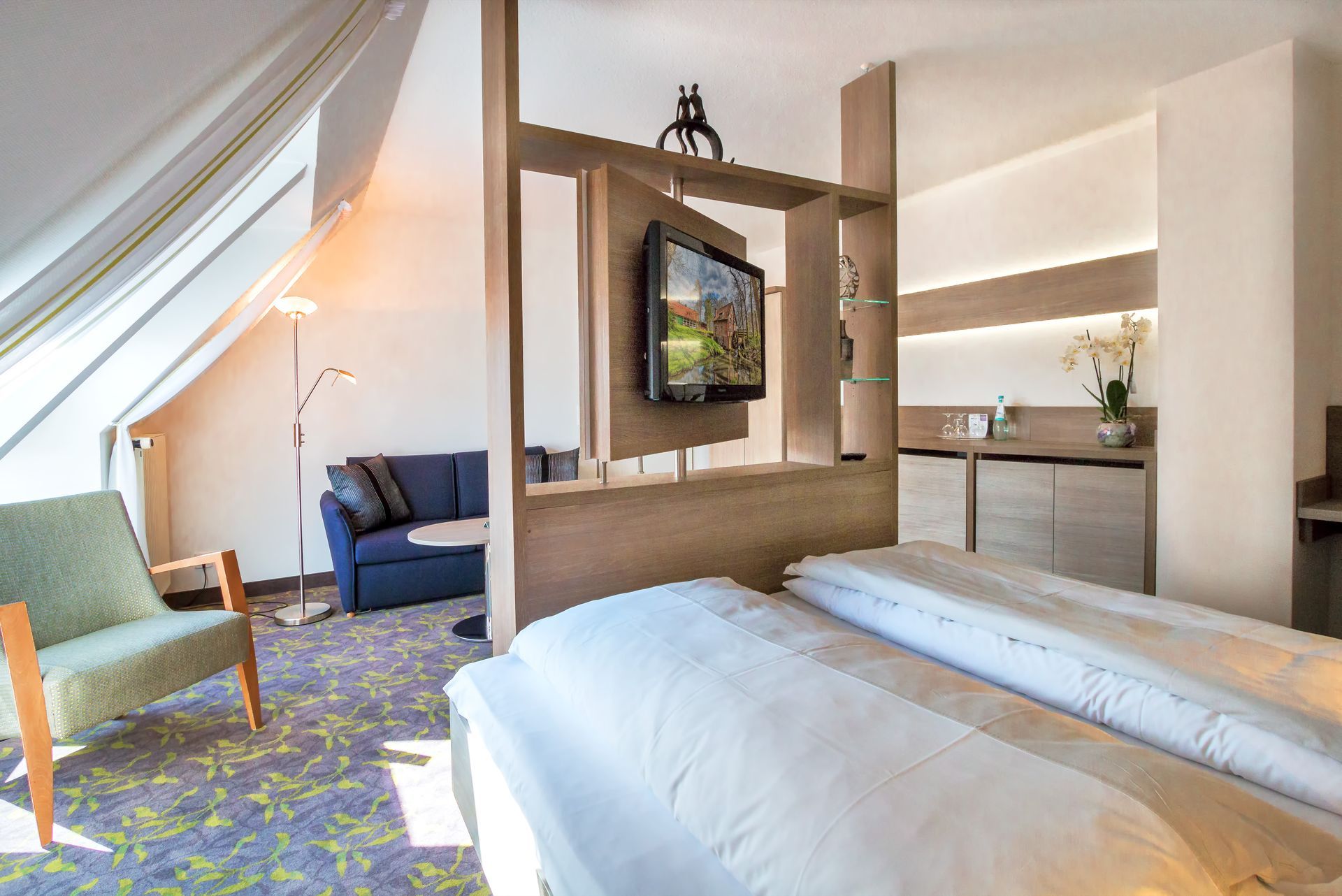 Ein Hotelzimmer mit Bett, Sessel, Couch und Fernseher.