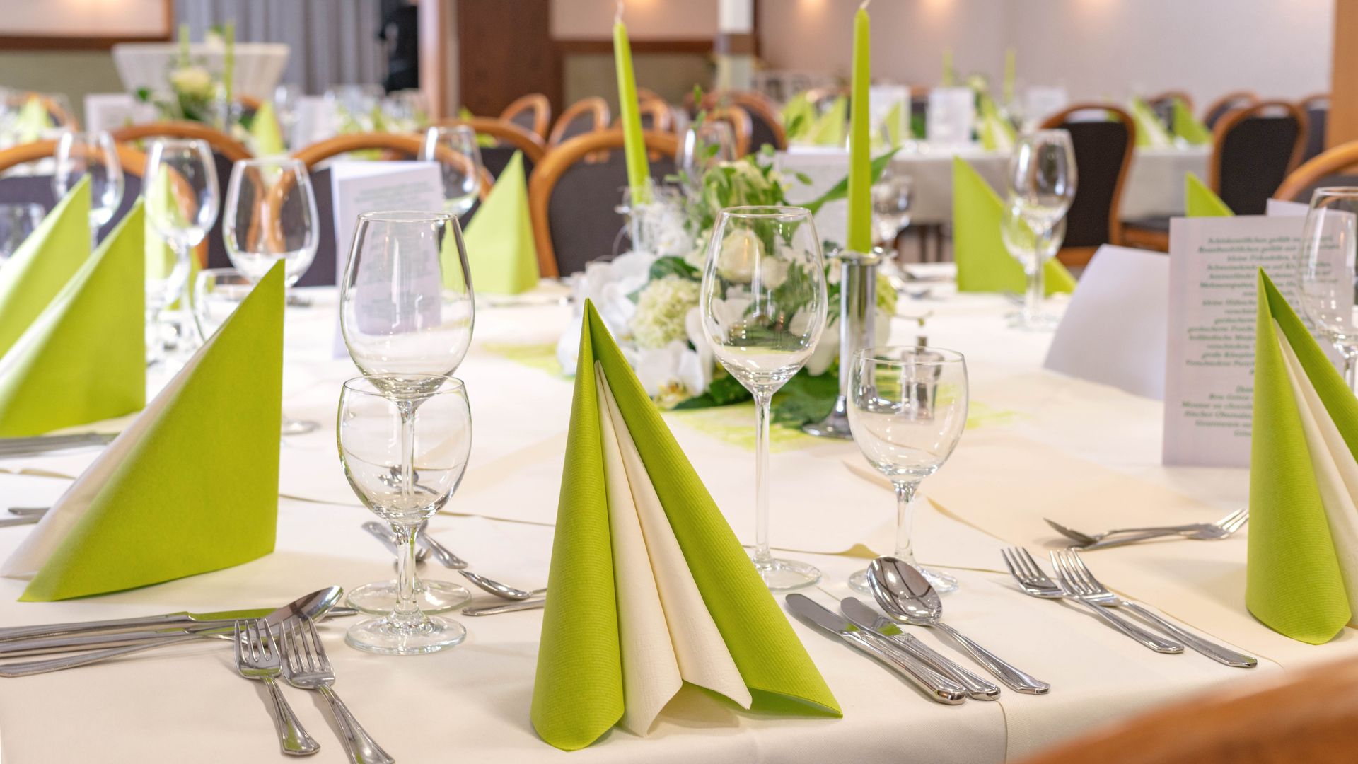 Ein Tisch ist für eine Dinnerparty mit grünen Servietten und Besteck gedeckt.
