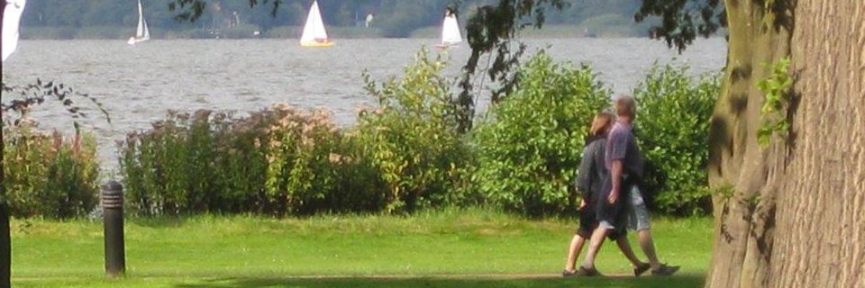 Ein Paar spaziert durch einen Park mit Segelbooten im Hintergrund