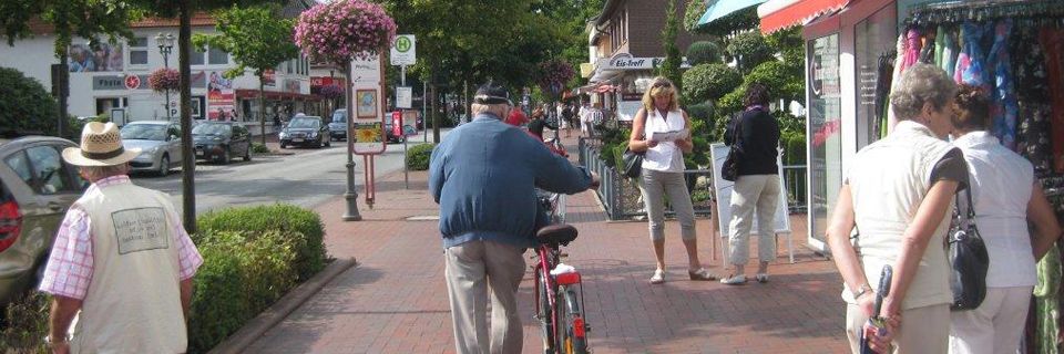 Eine Gruppe von Menschen geht mit einem Mann auf einem Fahrrad einen Bürgersteig entlang