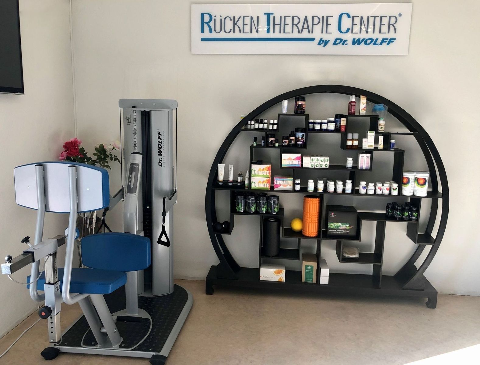 Die Eingangshalle des Therapiezentrums ist mit einem Aufstehsessel und einem runden Ausstellungsregal mit Produkten unter einem Schild ausgestattet.