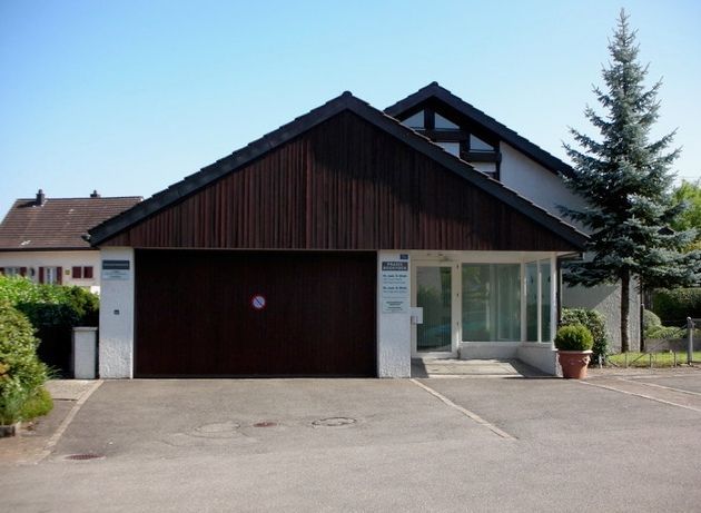 Eingeschossiges Haus mit dunklem Garagentor, weissen Fenstern und einer Auffahrt unter klarem Himmel