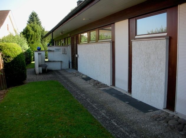 Schmaler Seitenhof neben einem Haus mit Kiesweg, Rasenfläche und Gartengeräten.