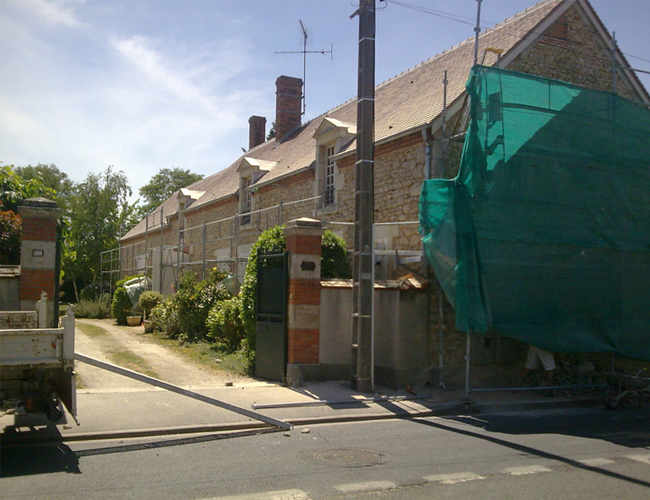 Rangée de maisons en briques derrière un portail, avec un filet de chantier vert sur le côté droit.