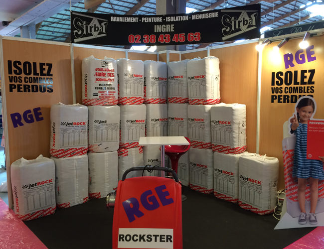 Stand d'exposition avec rouleaux d'isolant blanc empilés et signalétique rouge RGE Rockster pour l'isolation des combles.