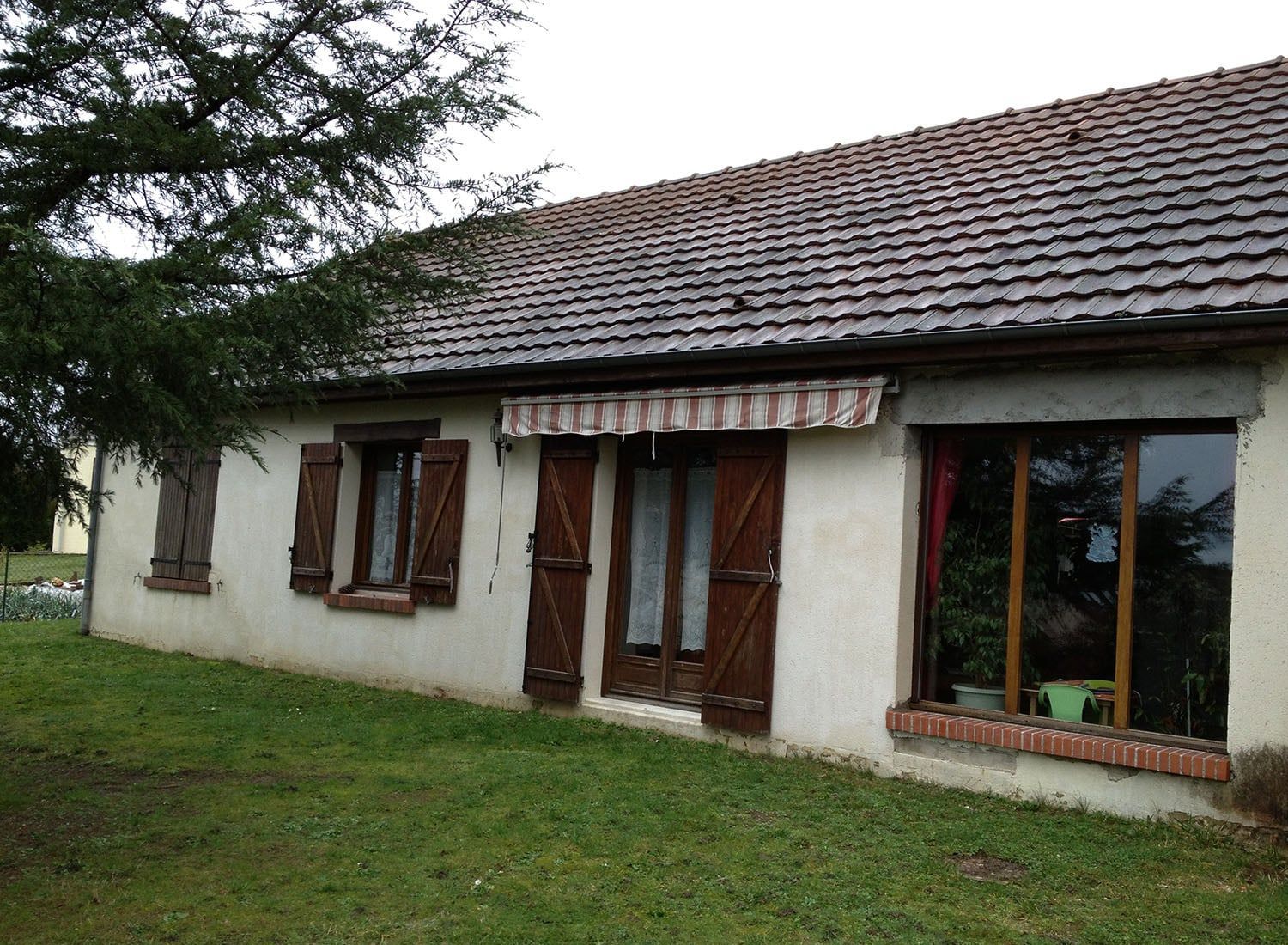 Maison de plain-pied avec murs blancs, volets marron, toit de tuiles et jardin gazonné