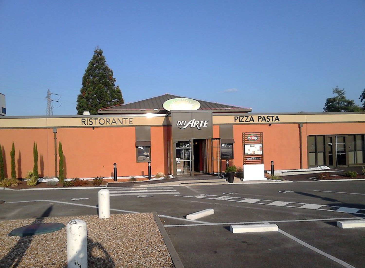Extérieur d'un restaurant-pizzeria aux murs orange et parking devant.