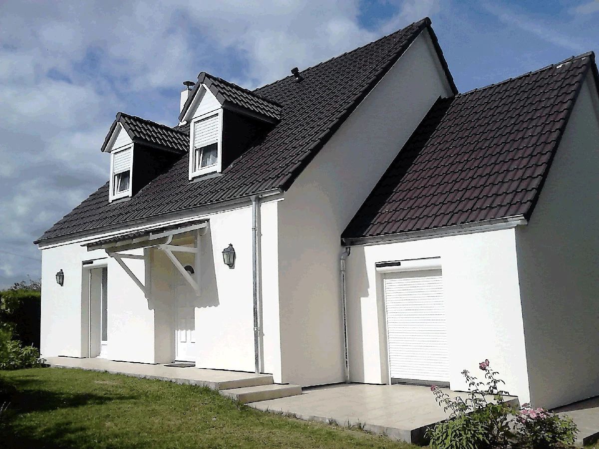Maison blanche au toit gris foncé, lucarnes et garage attenant sous un ciel bleu clair