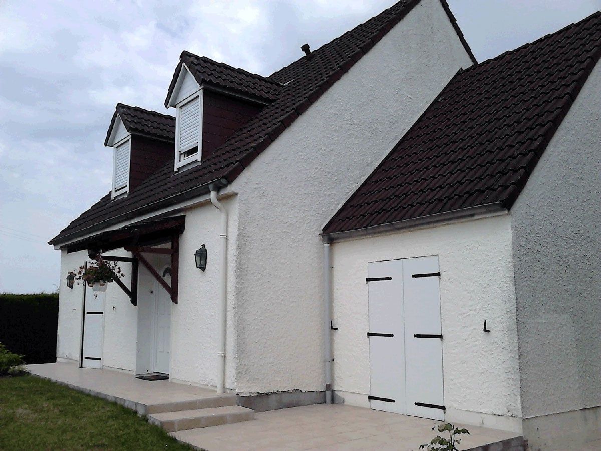 Maison de banlieue blanche avec toit sombre, entrée principale et portes de garage sous un ciel couvert