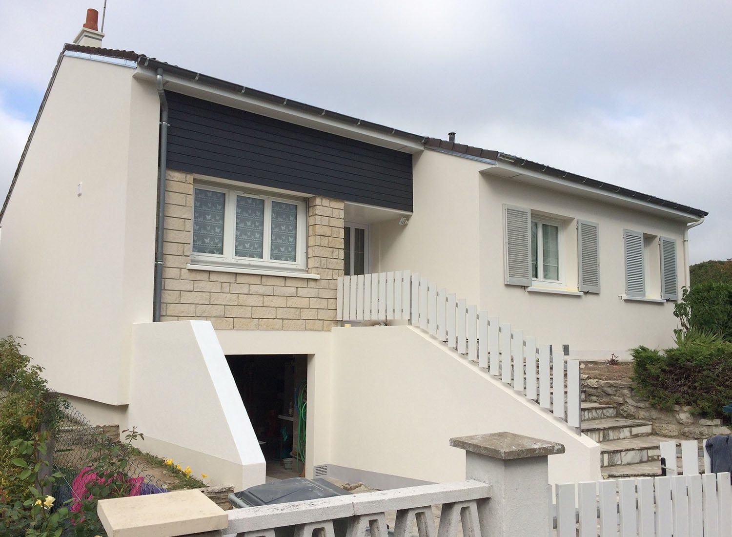 Extérieur d'une maison blanche avec façade en pierre, marches d'entrée et balustrade blanche sous un ciel nuageux