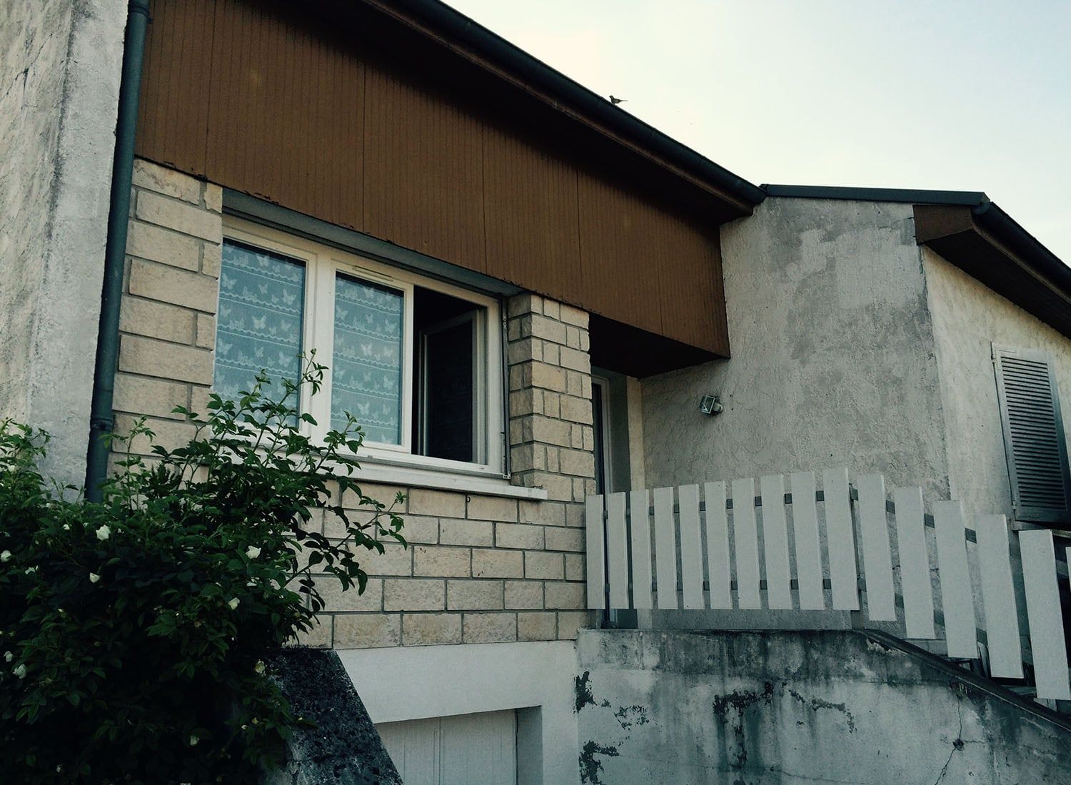 Extérieur d'une maison aux murs de pierre et blancs, avec une fenêtre et un toit en pente.